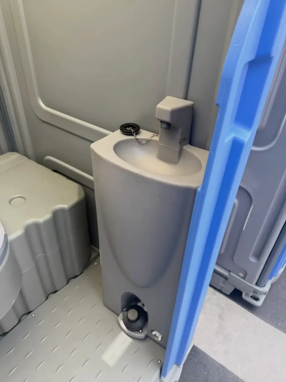 Inside a deluxe porta potty showing a fresh-water sink with foot pump