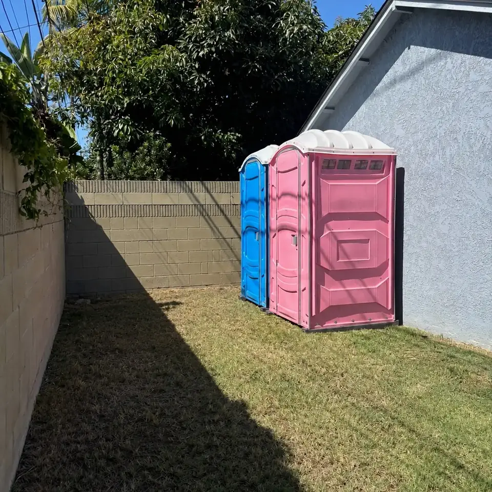 Pink and blue porta potties set in a fenced backyard for a party