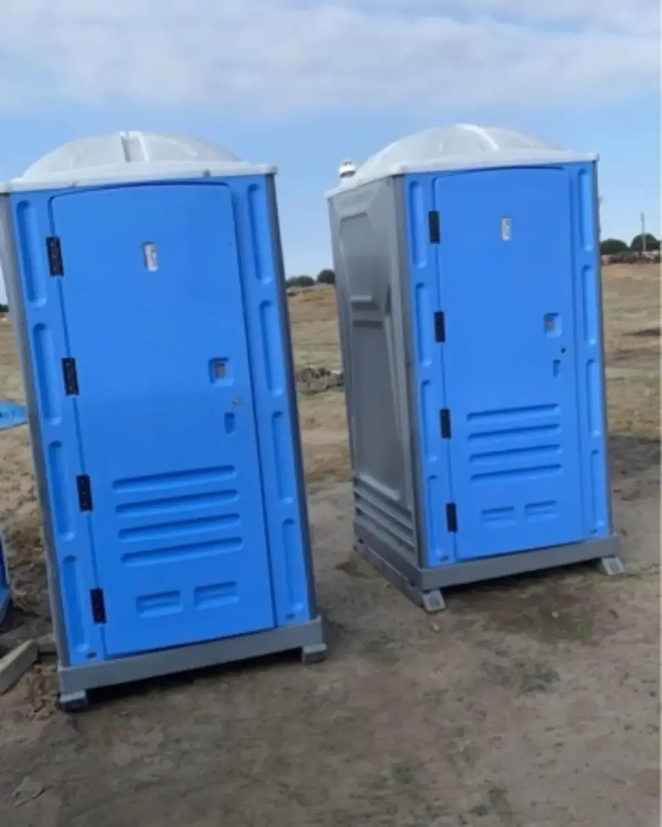 Two standard porta potties on a graded construction lot