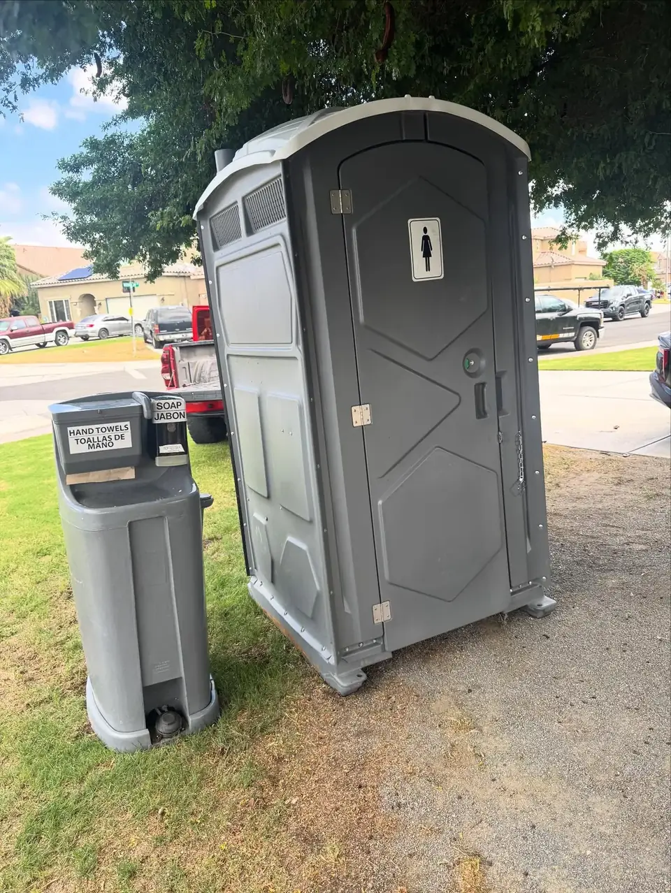 Gray standard porta potty with a hand wash station set up on a grass lawn